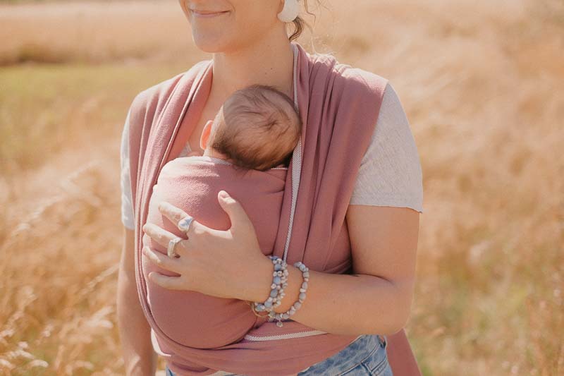zoom sur un bébé porté par sa maman , dans une écharpe néonulle terracotta dans un champ de blé. ateliers portage Maine et Loire 49 ou en visio, consultations allaitement, sommeil, portage et doula
