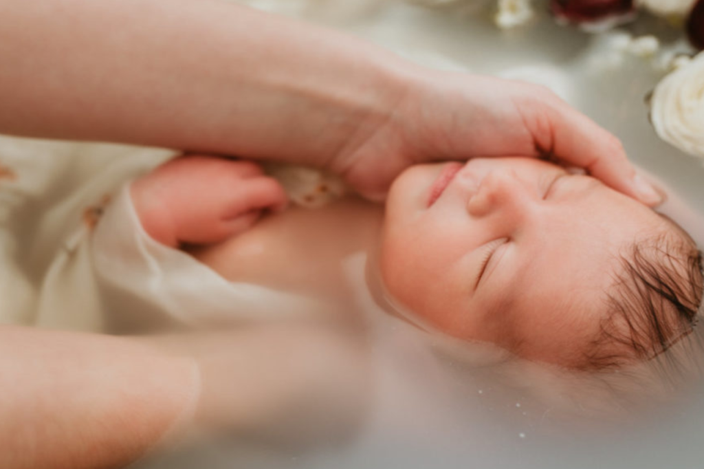 zoom sur le visage d'un bébé endormi dans le bain, apaisé, avec la tête qui repose dans la main d'une femme, bon cadeau de naissance - bain enveloppé bébé - bain renaissance - bain thalasso bébé - idée cadeau naissance bébé